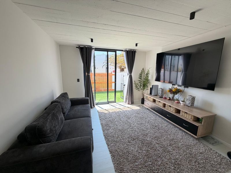 A bright living room featuring a modern exposed beam ceiling, track lighting, and a sliding glass door providing direct access to the outdoor area.