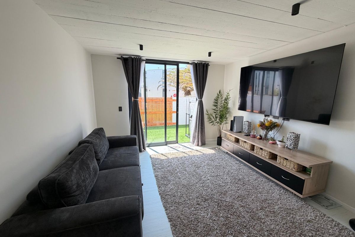 A bright living room featuring a modern exposed beam ceiling, track lighting, and a sliding glass door providing direct access to the outdoor area.