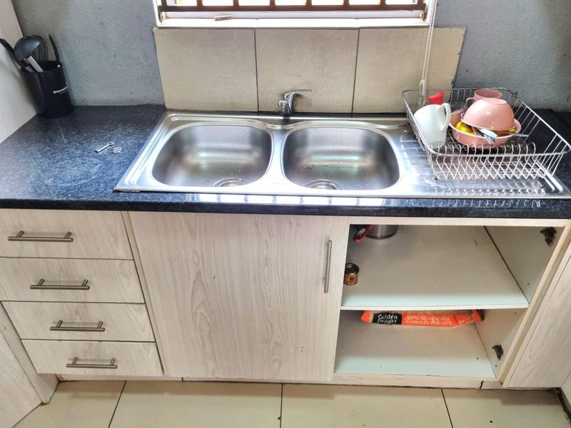 Kitchen sink area featuring a double bowl stainless steel sink, laminate countertop, and built-in cabinetry with a missing lower cabinet door.