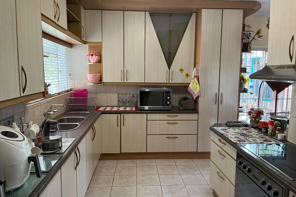 A functional kitchen featuring light-toned laminate cabinetry, tiled flooring, a double bowl sink, and integrated cooking appliances with a tiled backsplash.