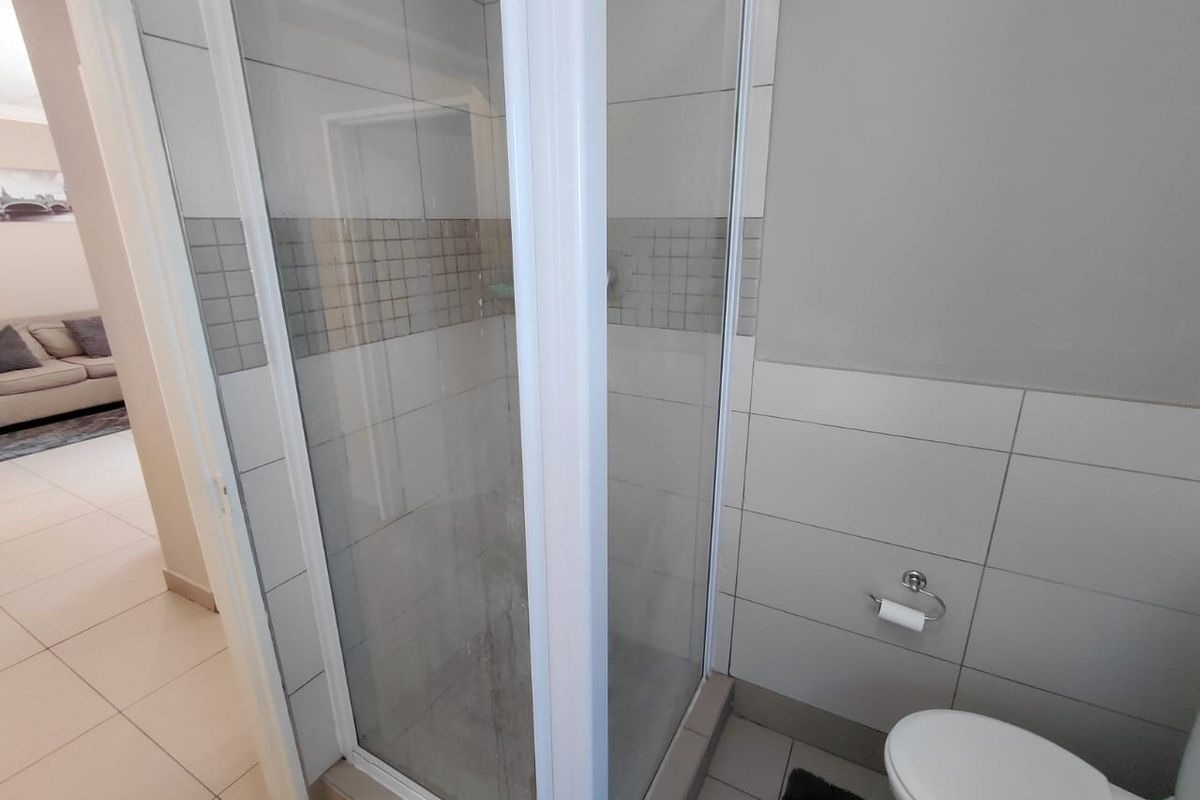 A functional bathroom featuring a glass-enclosed shower with tiled walls and a standard toilet, showing signs of wear on the shower glass.