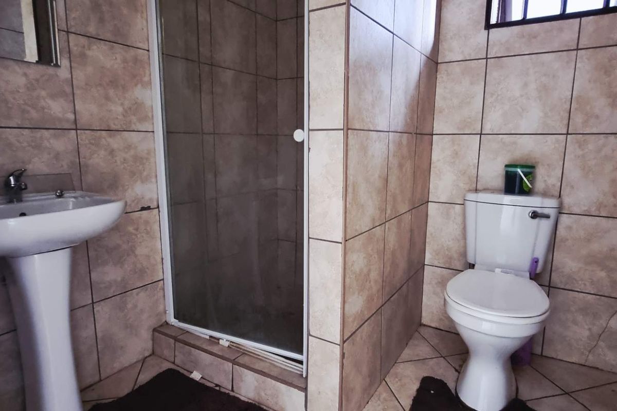 A functional bathroom featuring a pedestal basin, a tiled shower enclosure with a glass door, and a standard toilet.