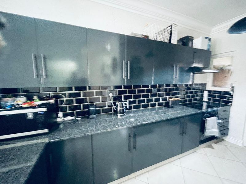 Modern kitchen featuring dark cabinetry, granite countertops, and a stylish subway tile backsplash with integrated electric hob and extractor fan.