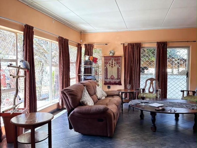 A spacious living room featuring large windows with security gates, tiled flooring, and a drop ceiling, offering potential for a modern update.