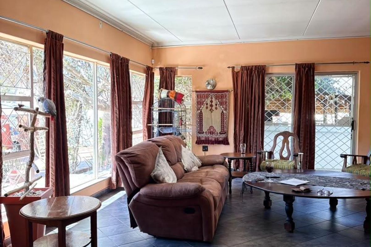 A spacious living room featuring large windows with security gates, tiled flooring, and a drop ceiling, offering potential for a modern update.