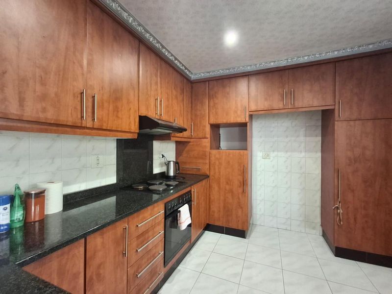 A functional kitchen featuring wood-look laminate cabinetry, granite countertops, built-in oven, electric hob, and tiled finishes throughout.