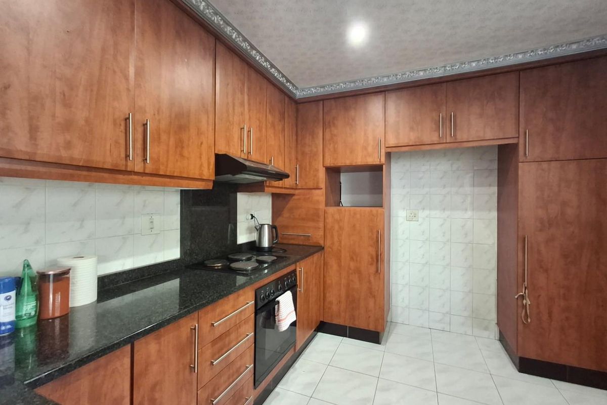 A functional kitchen featuring wood-look laminate cabinetry, granite countertops, built-in oven, electric hob, and tiled finishes throughout.