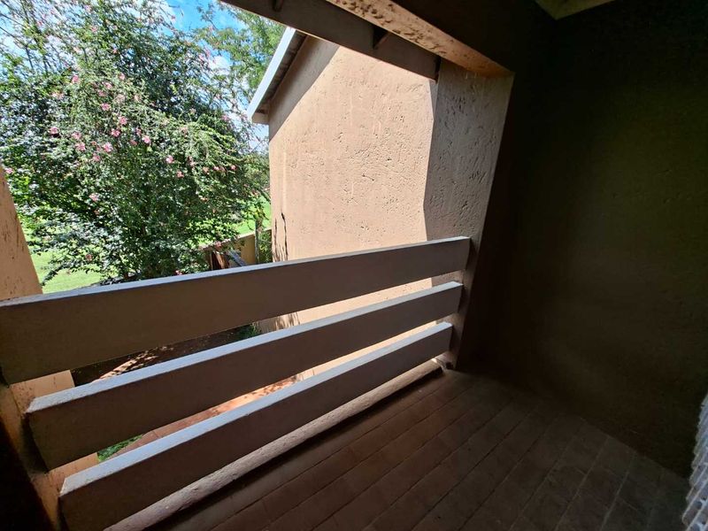 A covered balcony featuring a timber balustrade and tiled flooring, offering an outdoor space with views of the surrounding greenery.