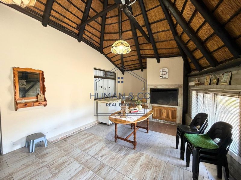 Spacious living area featuring a traditional thatched roof with exposed timber rafters, tiled flooring, and a built-in fireplace.