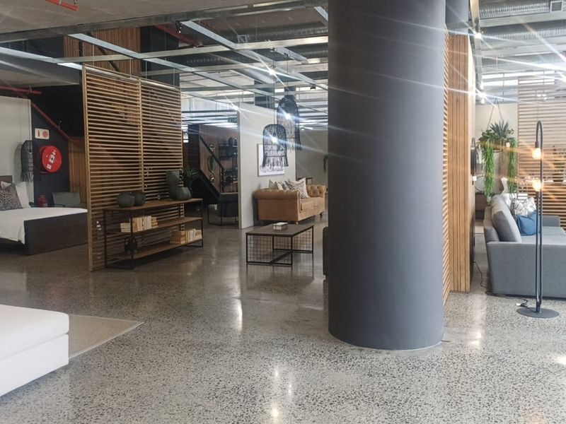 Spacious open-plan retail showroom featuring polished concrete floors, exposed industrial ceiling elements, and modern timber slat partitions creating distinct display zones.