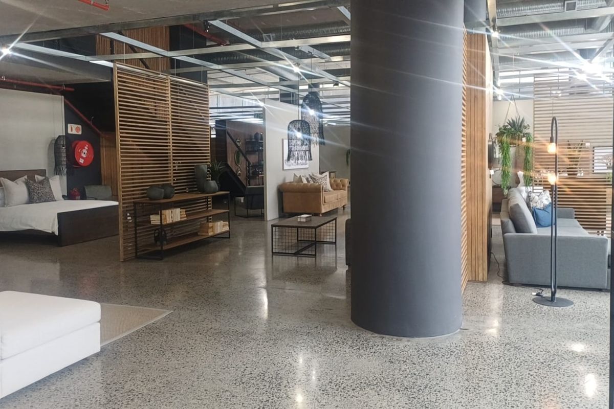Spacious open-plan retail showroom featuring polished concrete floors, exposed industrial ceiling elements, and modern timber slat partitions creating distinct display zones.