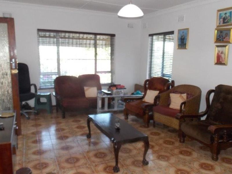 A living room featuring tiled flooring, coved ceilings, and large windows with venetian blinds, offering a functional and well-lit space.