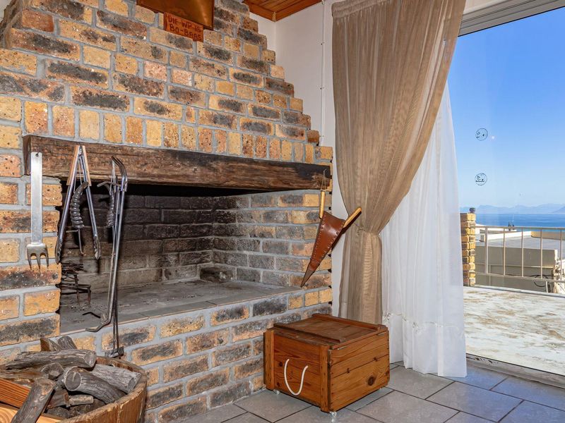 Living area featuring a rustic built-in brick fireplace with timber mantelpiece and large sliding glass doors opening to a balcony with ocean views.