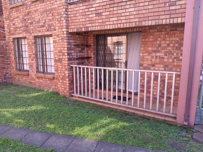 Ground floor patio area featuring a brick facade, metal security gate, and a simple balustrade overlooking a small garden space.