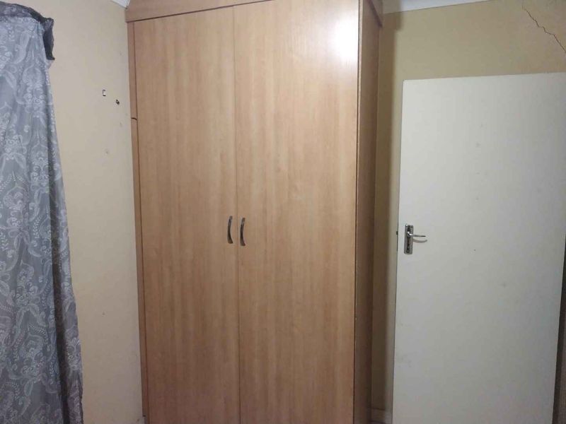 A bedroom interior featuring a built-in wooden wardrobe and a standard internal door, showing visible signs of wall cracking and surface wear.