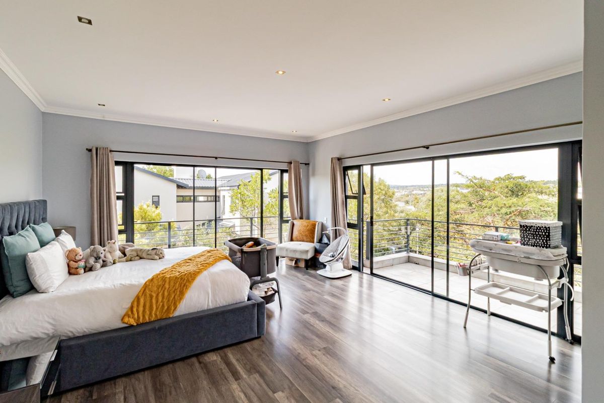 Spacious bedroom featuring modern laminate flooring, recessed lighting, and large sliding glass doors that open onto a private balcony with scenic views.
