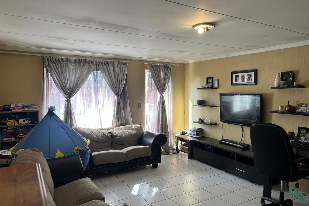 A living room featuring tiled flooring, wall-mounted shelving, and natural light through large windows with curtain rods.