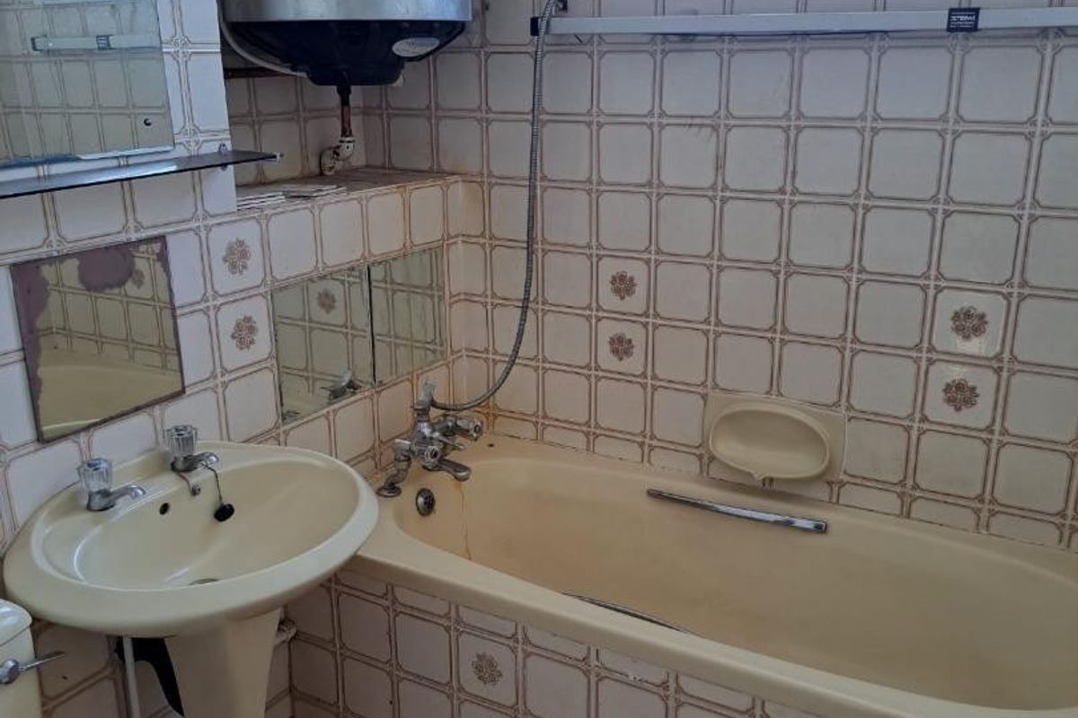A dated bathroom featuring a pedestal basin, bathtub, and wall-mounted water heater, finished with original wall and floor tiling.