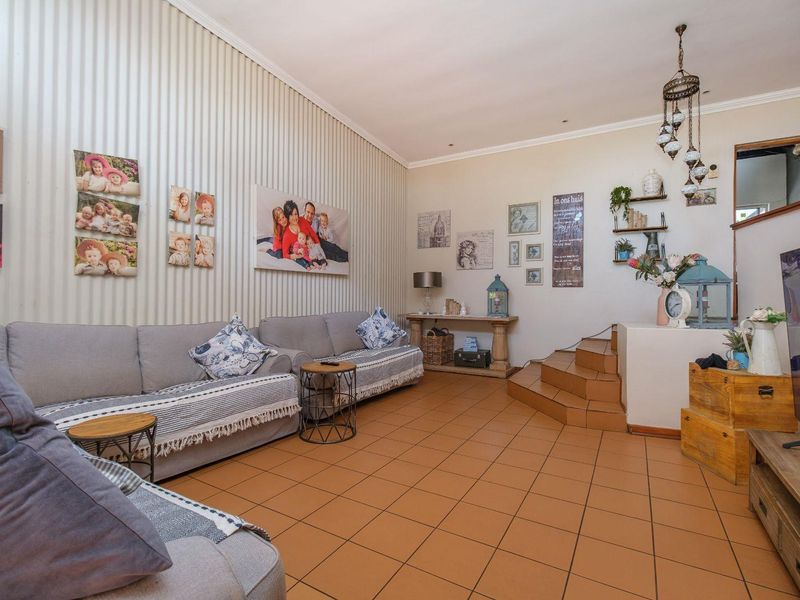 A spacious living room featuring tiled flooring, textured wall paneling, and a raised platform area, offering a versatile layout for comfortable family living.