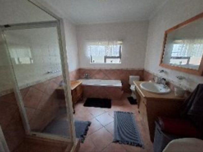 A functional bathroom featuring a glass shower enclosure, a built-in bathtub, a vanity cabinet with a basin, and tiled finishes throughout.