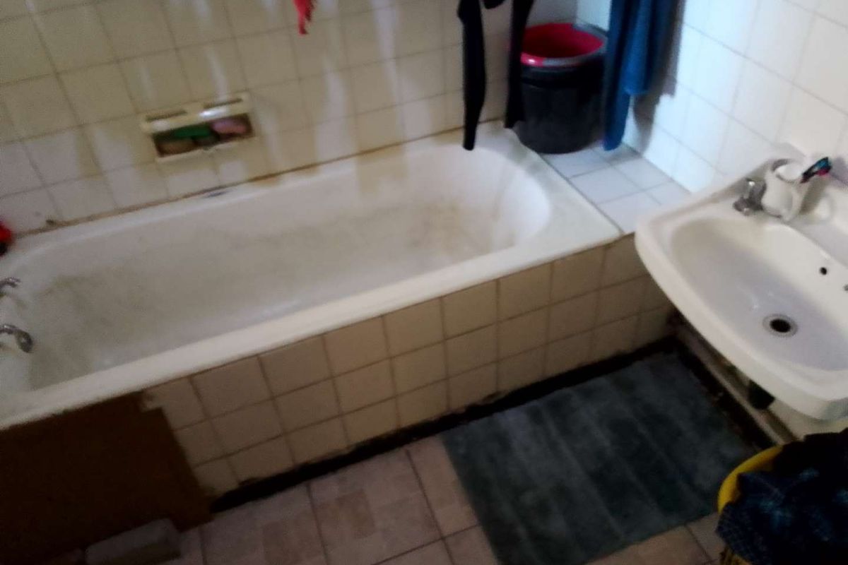 A functional bathroom featuring a built-in bathtub with tiled surround and a wall-mounted basin.