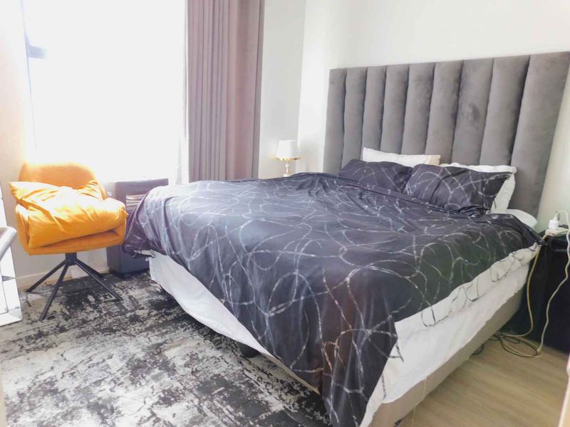 A well-lit bedroom featuring laminate flooring and a large window with curtain tracks, providing a comfortable and functional living space.