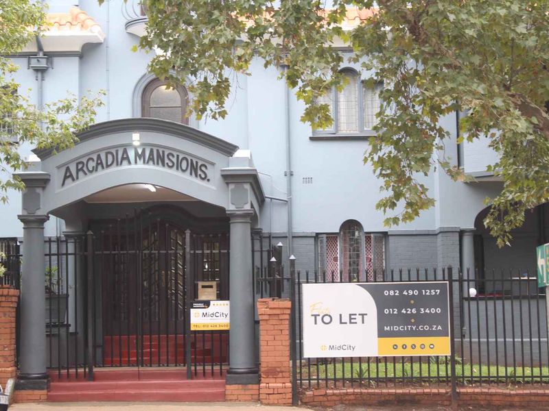 Front facade of Arcadia Mansions featuring an arched entrance portico, wrought iron security gates, and traditional architectural detailing.