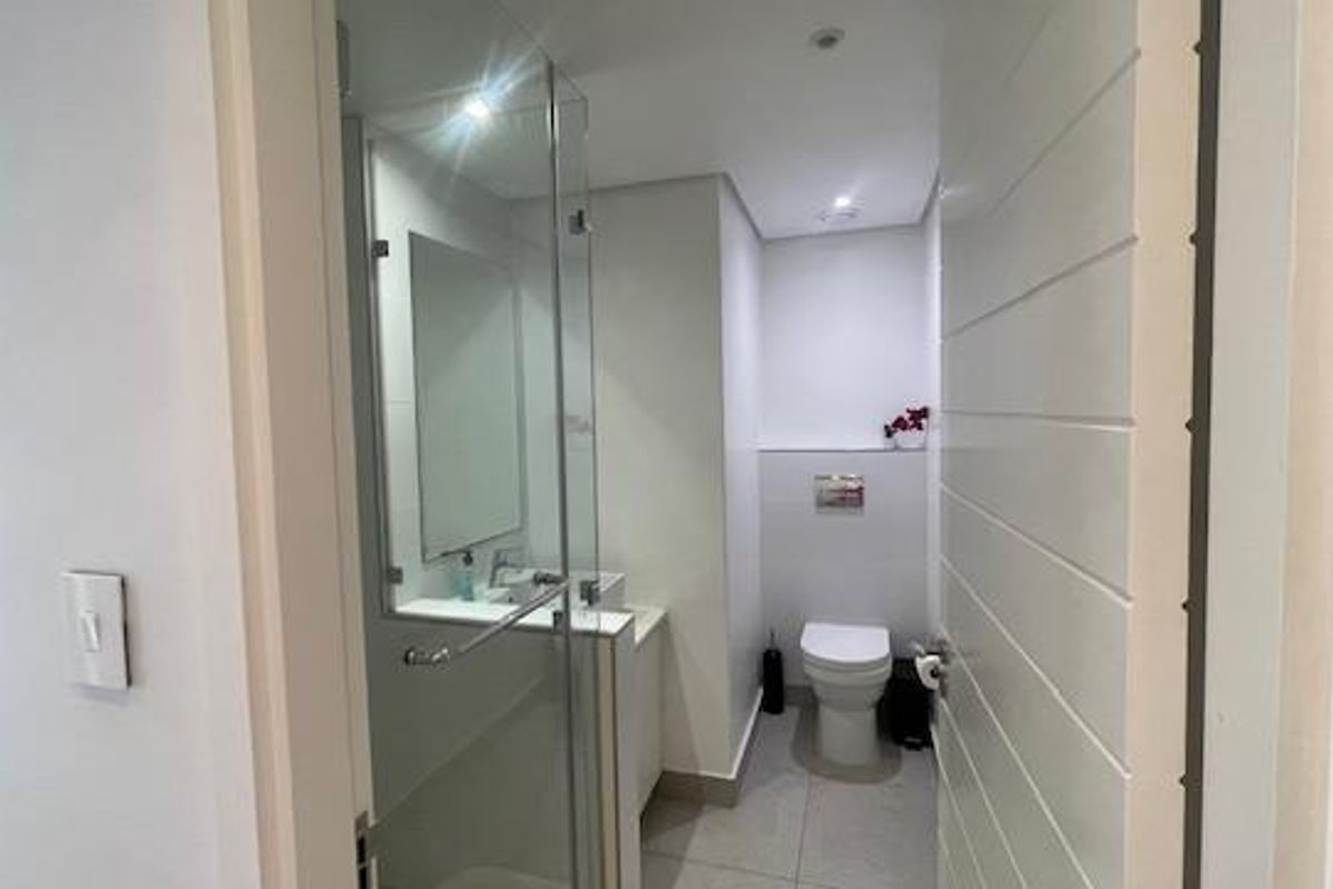 A modern, clean bathroom featuring a glass-enclosed shower, wall-mounted toilet, and a vanity basin with a mirror.