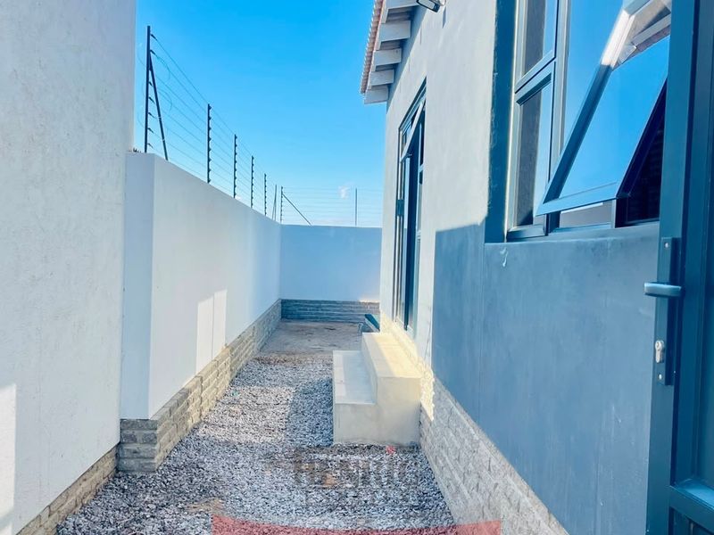 A side exterior passage featuring a gravel pathway, concrete steps, and secure boundary walls with electric fencing.