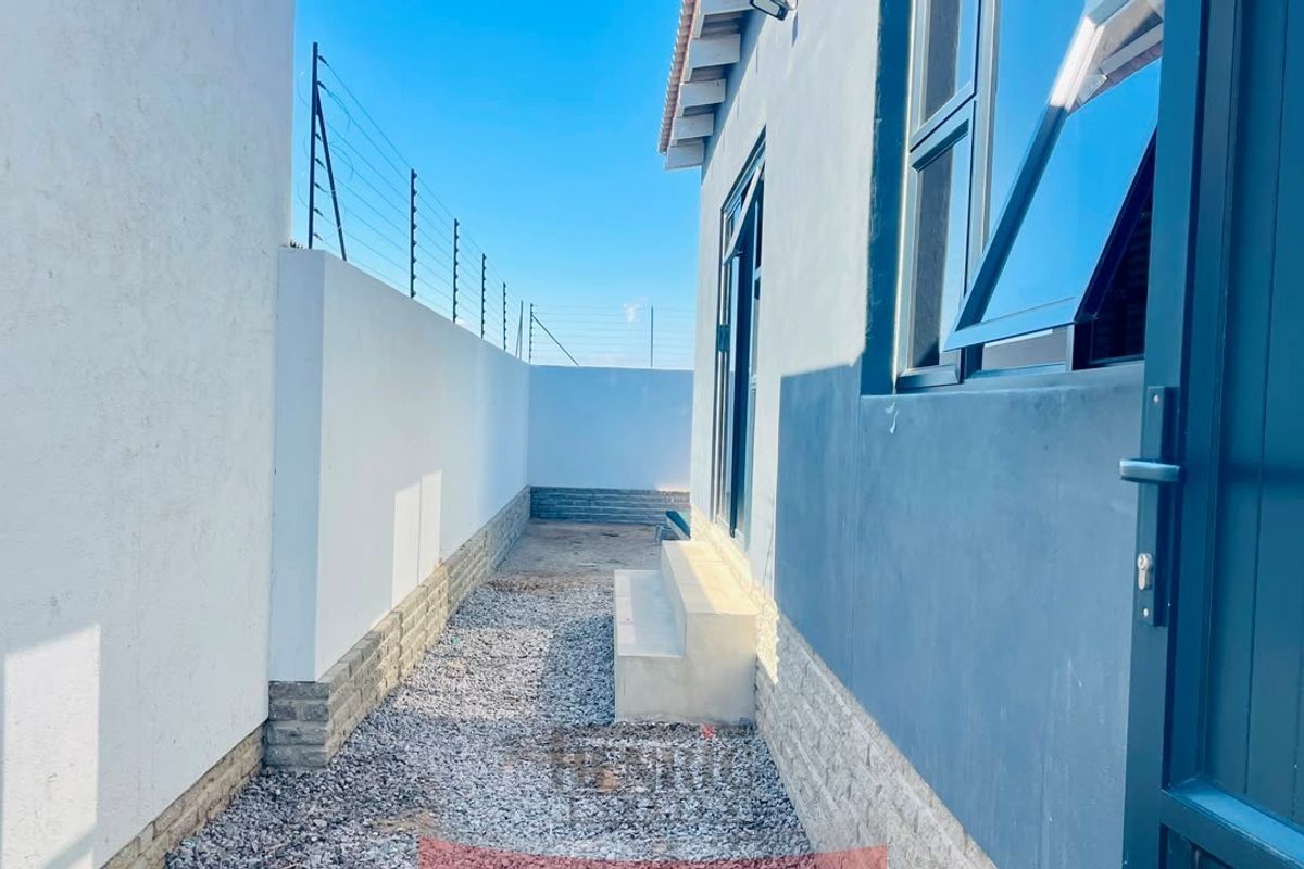 A side exterior passage featuring a gravel pathway, concrete steps, and secure boundary walls with electric fencing.