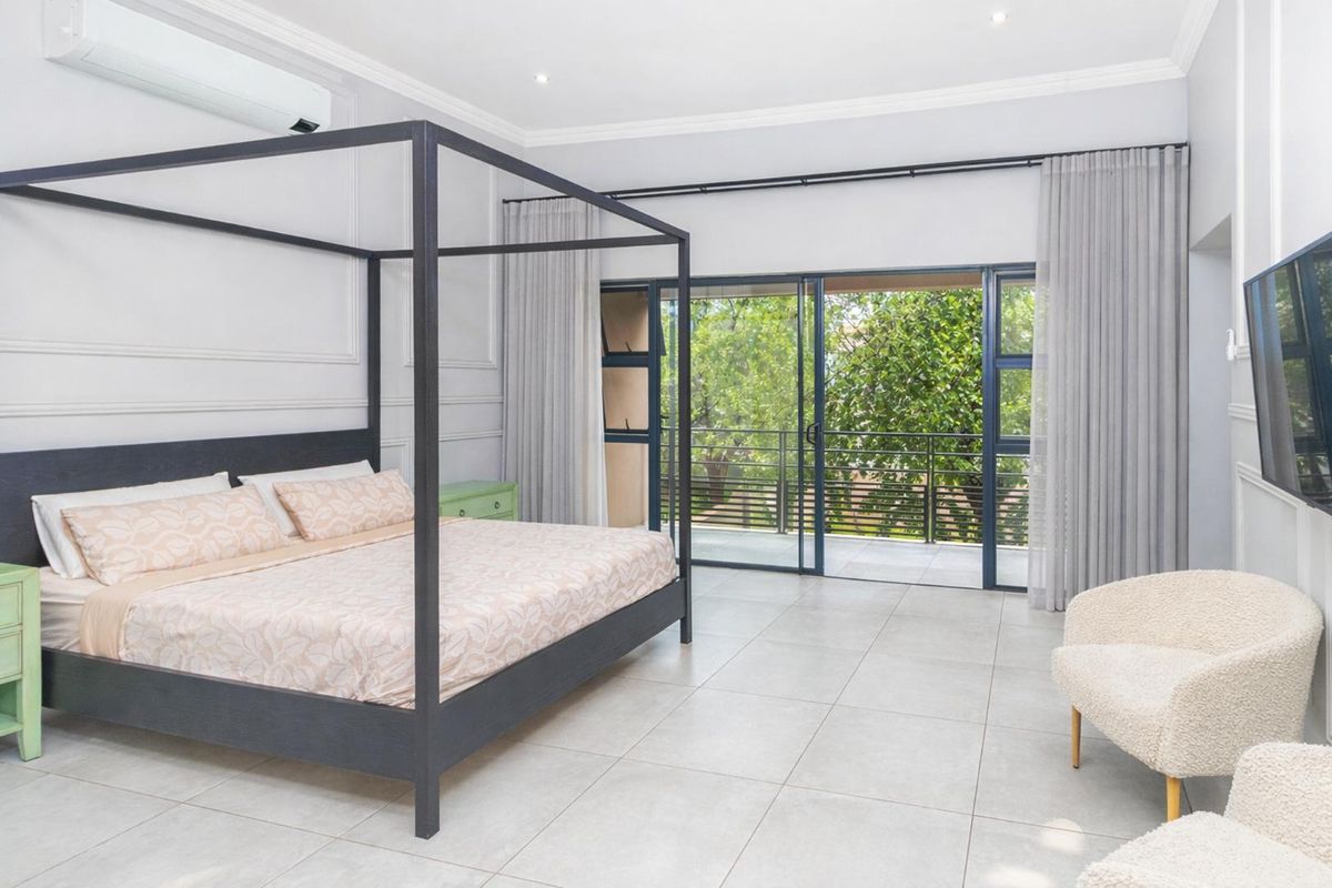 Spacious bedroom featuring elegant wall paneling, crown molding, tiled flooring, and large sliding glass doors that open onto a private balcony.