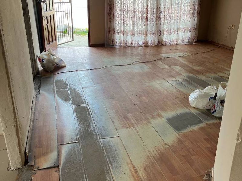 An empty living room featuring worn laminate flooring and exposed ceiling joists, with access to an exterior security gate and sliding door.