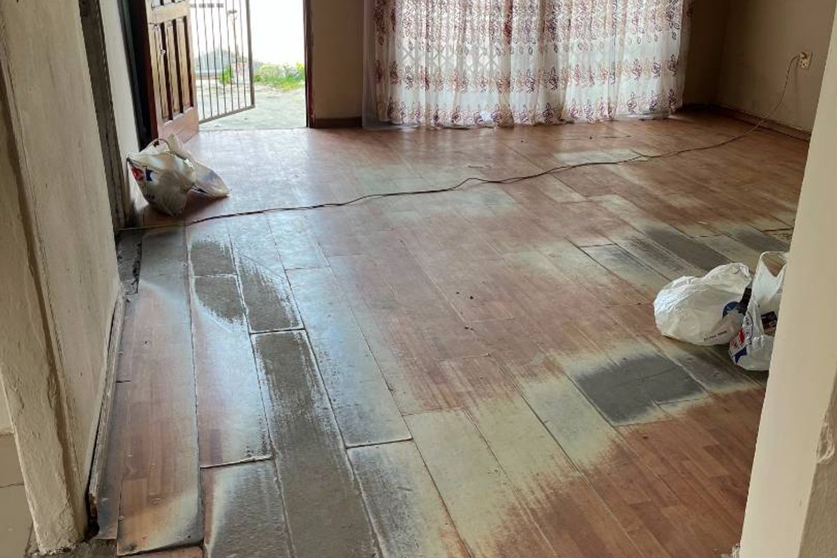 An empty living room featuring worn laminate flooring and exposed ceiling joists, with access to an exterior security gate and sliding door.
