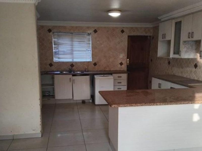A dated kitchen featuring granite countertops, built-in cabinetry, and a breakfast bar, currently empty and in need of cosmetic updates.