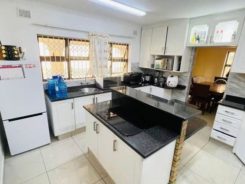 A functional kitchen featuring white cabinetry, granite countertops, a central island with a built-in hob, and tiled flooring.