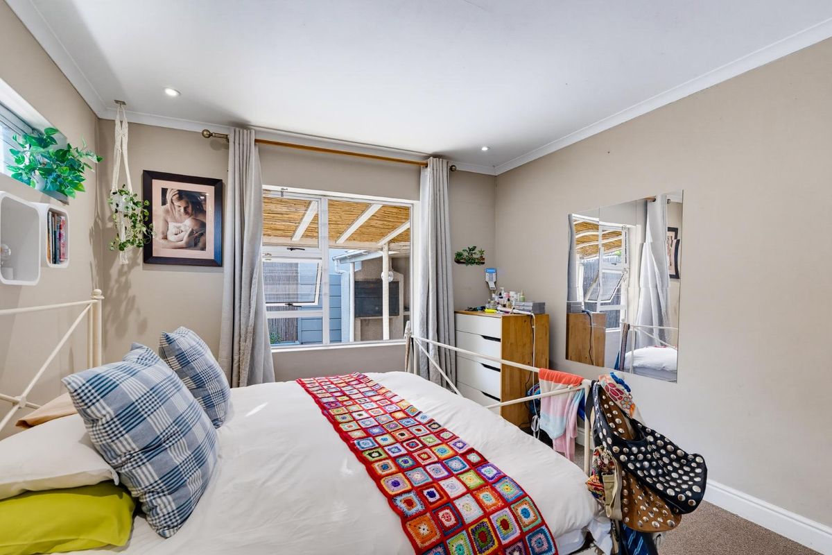A well-lit bedroom featuring neutral wall tones, recessed downlights, and aluminium-framed windows with views to the outdoor patio area.