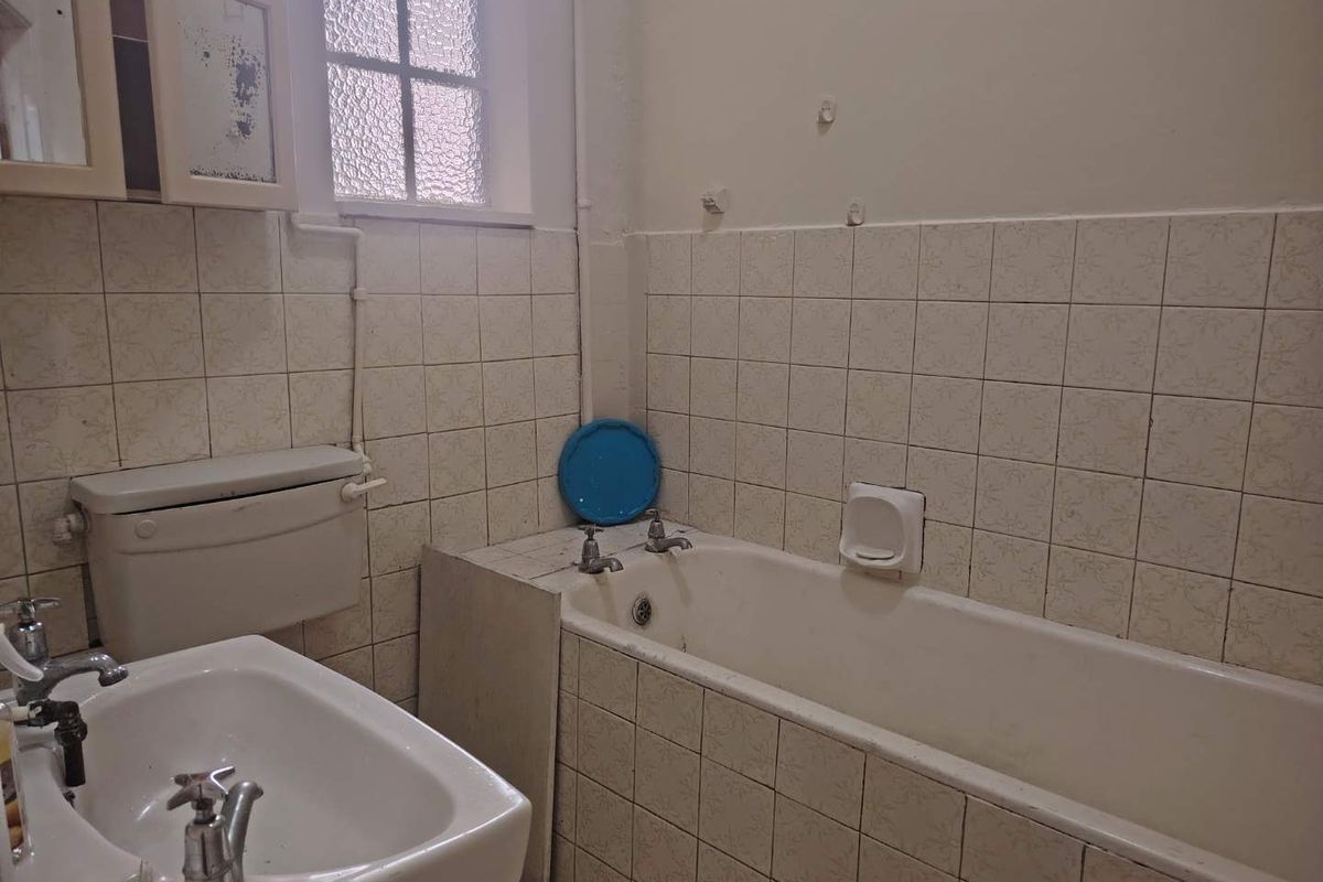 A dated bathroom featuring original wall tiling, a standard bathtub, and a pedestal sink, requiring modernization and cosmetic updates.
