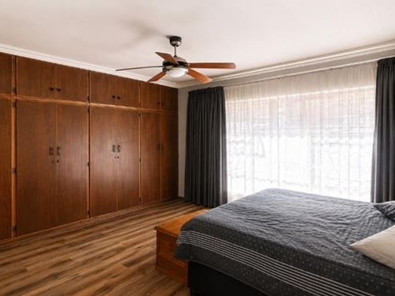 A spacious bedroom featuring extensive floor-to-ceiling built-in wooden cupboards, laminate flooring, and a ceiling fan, offering ample storage and a neutral aesthetic.