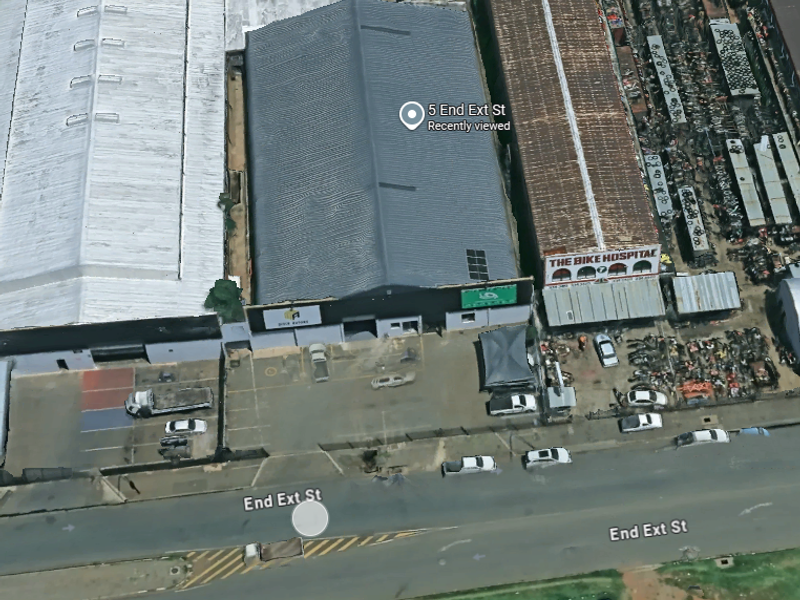 Aerial view of an industrial warehouse property featuring a large metal roof, paved parking area, and street-level access.