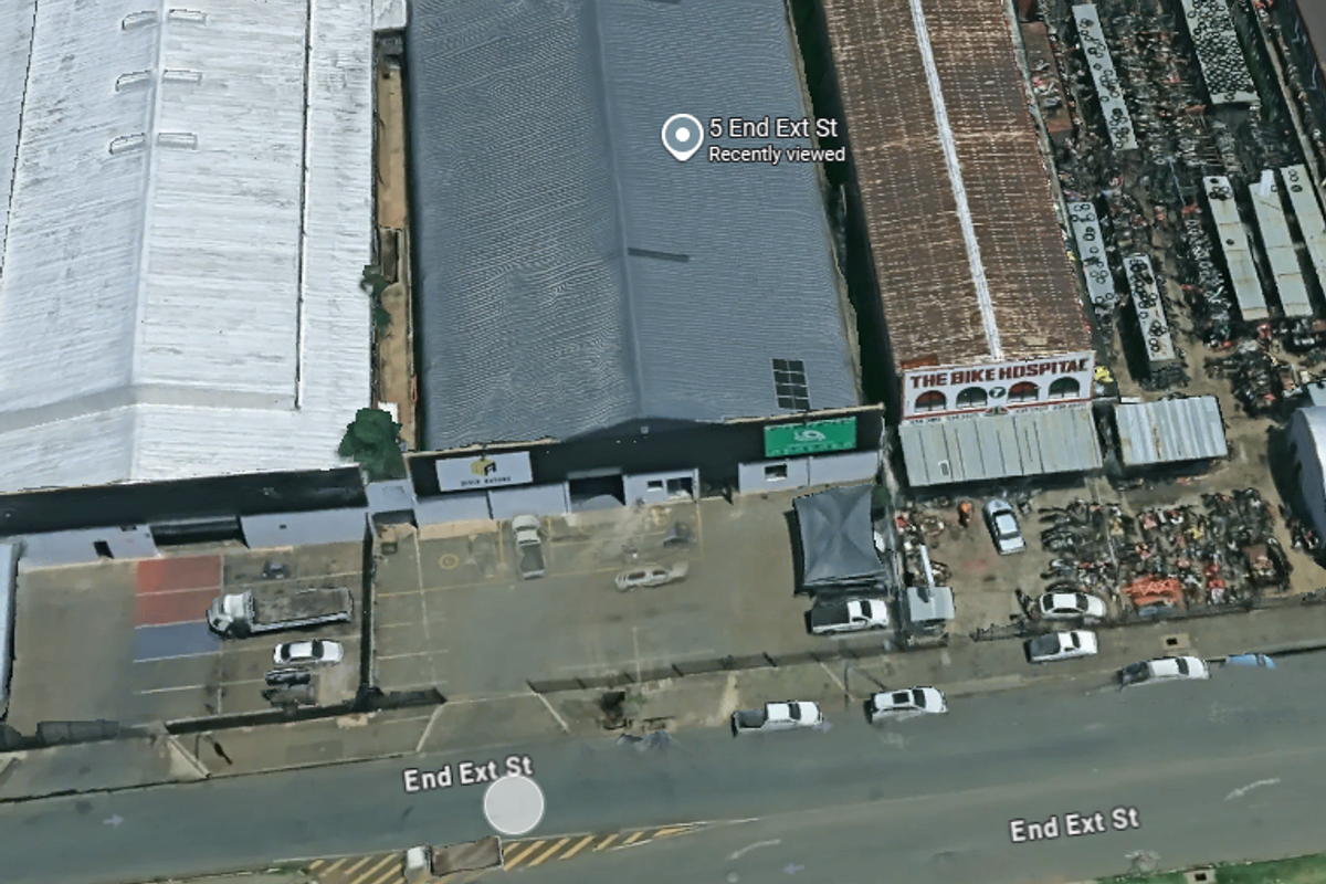 Aerial view of an industrial warehouse property featuring a large metal roof, paved parking area, and street-level access.