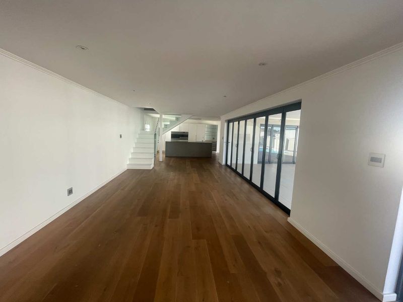 Spacious open-plan living area featuring hardwood flooring, a modern staircase with glass balustrade, and large bi-fold doors leading to the outdoor area.