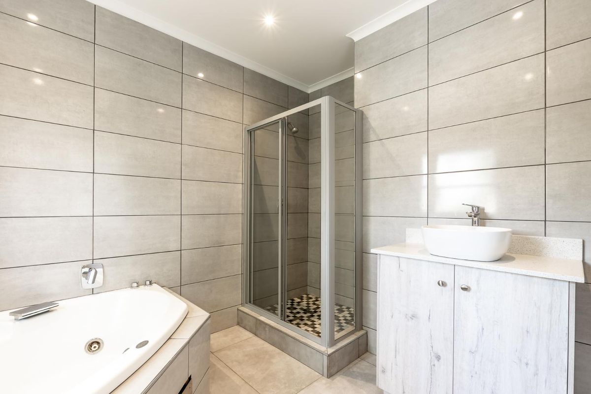 Modern bathroom featuring a corner bathtub, a separate glass-enclosed shower, and a vanity unit with a vessel sink, finished with neutral grey wall tiles.