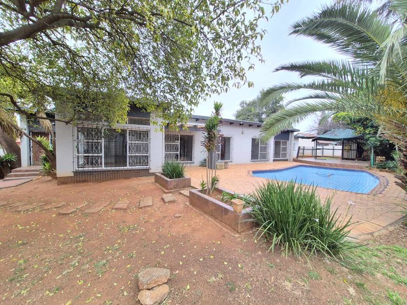 Rear exterior view featuring a swimming pool, paved patio area, and established garden with mature trees.