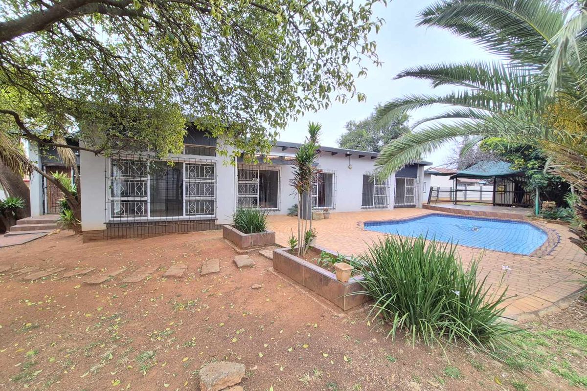 Rear exterior view featuring a swimming pool, paved patio area, and established garden with mature trees.