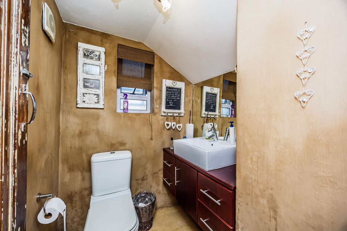 A compact bathroom featuring a vanity with a vessel sink, a toilet, and a small window, finished with textured wall treatments.