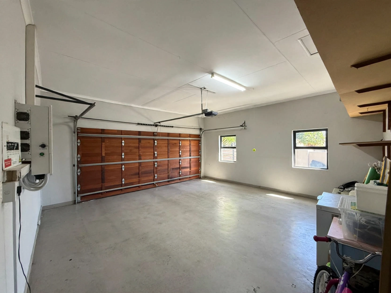Spacious double garage featuring a sectional wooden door, concrete flooring, built-in shelving, and an installed inverter system for power backup.
