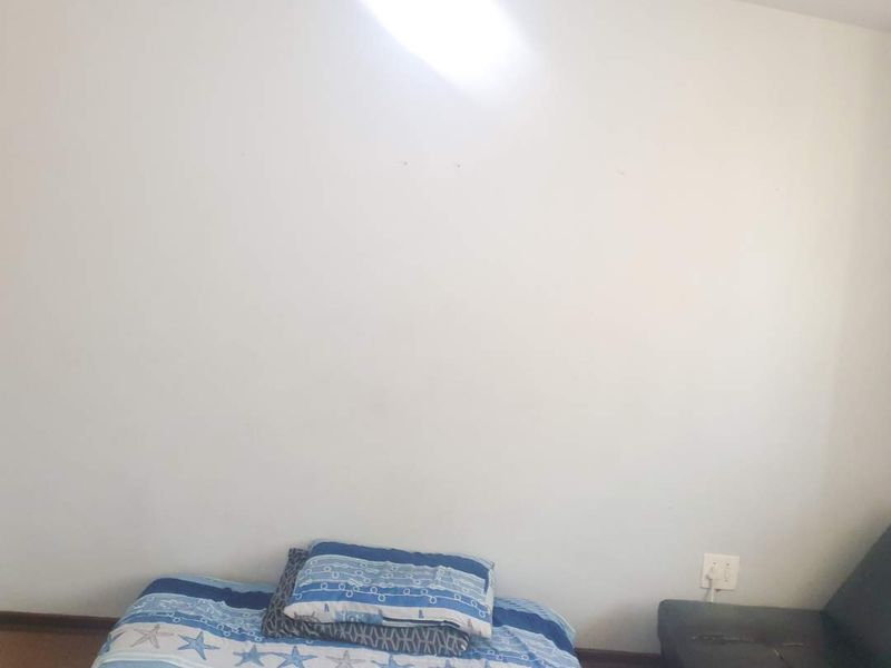 A simple bedroom space featuring neutral walls, a pendant light fixture, and an electrical outlet.