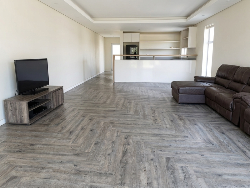 Spacious open-plan living area featuring modern herringbone flooring, recessed ceiling lights, and a functional kitchen with a breakfast bar island.