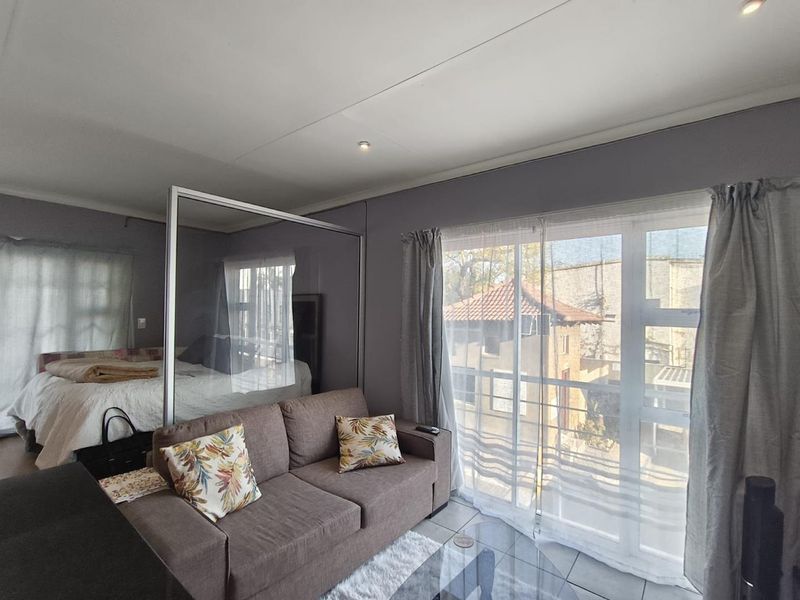 Open-plan living area featuring a glass room divider, tiled flooring, and large sliding doors providing access to a balcony.