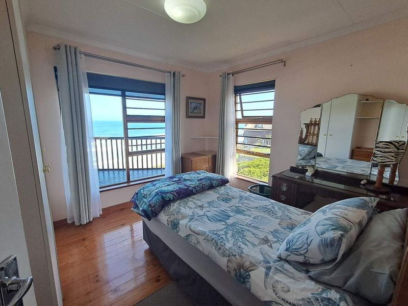 A bedroom featuring hardwood flooring, louvered windows, and direct access to a balcony with ocean views.